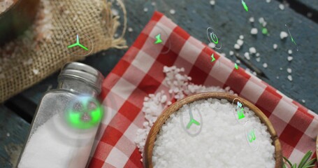 Displaying wooden bowl holding coarse salt on teal table with glass shaker and green icons