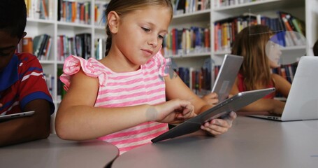Tapping central girl wearing pink-striped top using tablet at library with bookshelves and table
