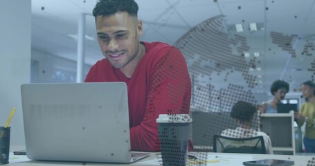 Leaning man in red long-sleeve top working on silver laptop at open-plan office, with coffee cup