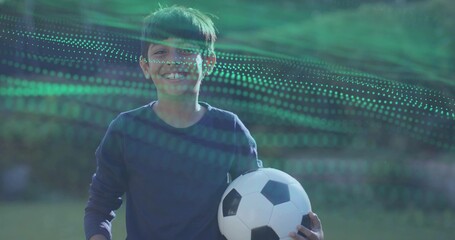 Smiling Indian-Asian boy holding soccer ball on sports field, wearing navy shirt with green overlay