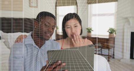 Leaning couple viewing tablet on bed, woman red camisole, man blue shirt, 3D wireframe cube