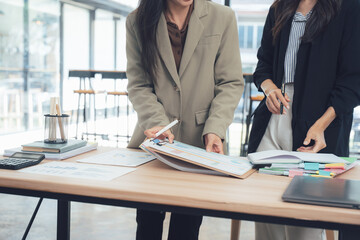Businesswomen in Discussion: Two stylish businesswomen engage in a productive discussion around a table, the focus is on a review of critical reports.