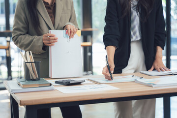 Businesswoman Duo Collaborating: Two professional women meticulously analyze data and strategies, engrossed in their work at a modern workspace. This image embodies partnership, expertise.