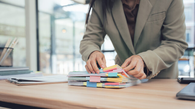 Organizing Documents: A focused individual meticulously organizes a stack of important documents on a wooden desk. Amidst the organized chaos, the individual sorts through the documents.