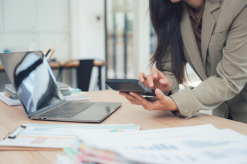 Analyzing Finances at Work: A professional woman focused on detailed financial analysis, with a calculator in hand, desk covered with paperwork and a laptop in the modern office. 