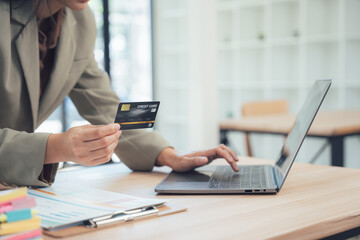 Online Transaction: A focused professional engaging in a seamless online transaction, utilizing a laptop and a credit card, set against the backdrop of a modern workspace.