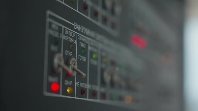 Close-up pan across industrial control panel with metal toggle switches and multicolored indicator LEDs, shallow depth of field emphasizing status lights and engraved labels on equipment interface
