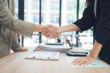 Handshake Deal: A close-up shot of two individuals shaking hands across a desk, representing an agreement or successful business deal, symbolizing partnership and cooperation.