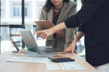 Collaboration in Office: Focused businesswomen collaborate over a laptop, discussing work-related topics with a professional ambiance.