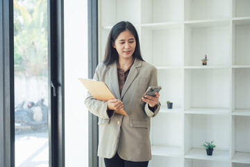 Professional Business Woman with Smart Phone: A poised business woman, dressed in a smart blazer, engaged with her smart phone while holding a file folder.