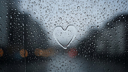 A heart drawn on a foggy window with raindrops on a gloomy day