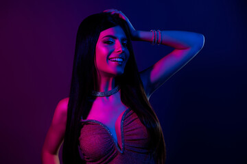 Stylish young woman in elegant evening wear posing under vibrant neon lights in a glamorous...