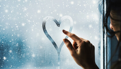 A hand drawn heart on the foggy window while it is snowing outside.