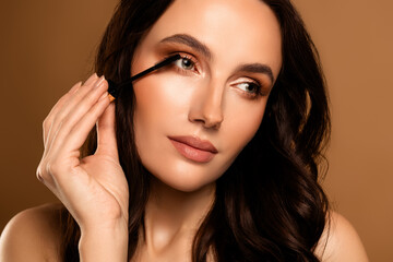 Beautiful young brunette woman applying mascara with a brush, showcasing an elegant and glamorous...