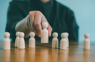 Hand selecting wooden figure from group on table, leadership and human resources concept, team management, recruitment decision, talent selection, business strategy and organization.