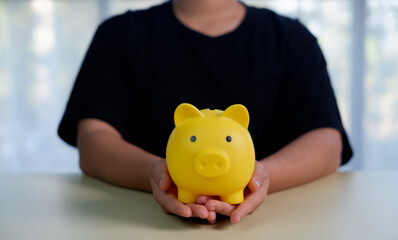 Hands holding a yellow piggy bank on a desk, symbolizing saving money, personal finance, smart budgeting, financial security, wealth management, future planning, and minimalist lifestyle.