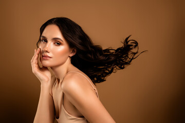 Beautiful young woman with flawless skin and elegant hairstyle posing against a beige background