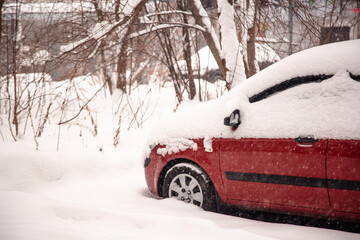 The red car is covered with a large snowdrift