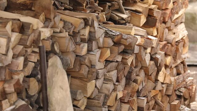 A large stack of chopped firewood logs arranged neatly outdoors. This rustic lumber pile serves as prepared natural fuel for winter heating in a fireplace or stove.

