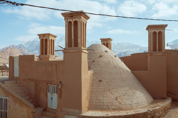Traditional windcatchers and a mud-brick dome stand against a stunning mountain backdrop,...