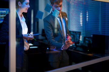 Professional corporate executives planning strategic business goals on whiteboard. Leadership team analyzing financial market trends and project workflow in modern office at night.