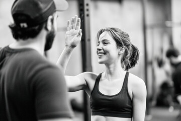 A cheerful interaction in a gym setting, showcasing a woman giving a high-five to a man, emphasizing fitness and camaraderie.