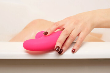 A woman takes a vibrator from the side of the bathroom while taking a bath