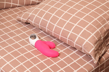 Pink curved vibrator resting on a checkered bedsheet beside a matching pillow