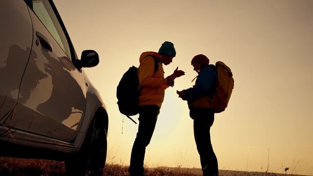 Two travelers check map near car as sunset silhouette frames couple with backpack standing by parked suv on grassy roadside during hiking adventure and roadtrip outdoors traveler planning route