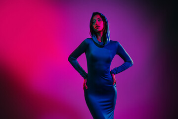 Portrait of a glamorous young woman wearing a blue hooded dress in vibrant neon pink and purple...
