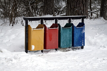 Row of colorful recycling bins standing in snowy winter forest front view closeup