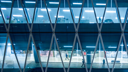 Modern glass office building interior seen through geometric facade in Hong Kong, China. Abstract corporate workplace with anonymous silhouettes symbolizing business activity and organization