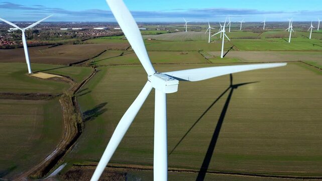 Close up aerial view of wind turbine, windmill for renewable energy generation, rising up shot, sunny winter skies in the United Kingdom.