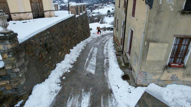 Snowy Italian village street with a person shoveling snow and a stone wall