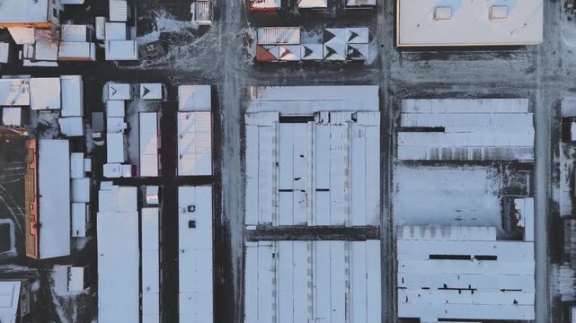 Drone hovering above a city marketplace, winter layout of stalls, pavilion rooftops, snow-covered ground and geometric aerial urban pattern