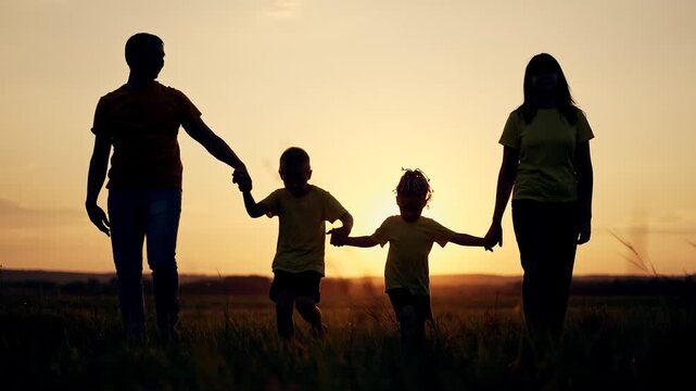 Family walking hand in hand across open field at sunset silhouette of parent mother father and child holding hand together in tall grass under warm orange sky slow stroll toward horizon with glow