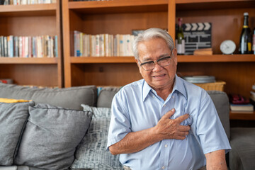 Senior man experiencing chest pain at home. Older man sitting on couch with hand on chest. Heart...