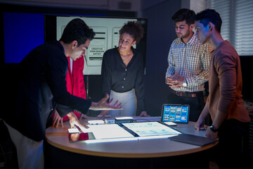 Creative UI/UX design team analyzing mobile app wireframes on illuminated digital touch table. Diverse developers brainstorming web layout strategy in modern high-tech office at night.
