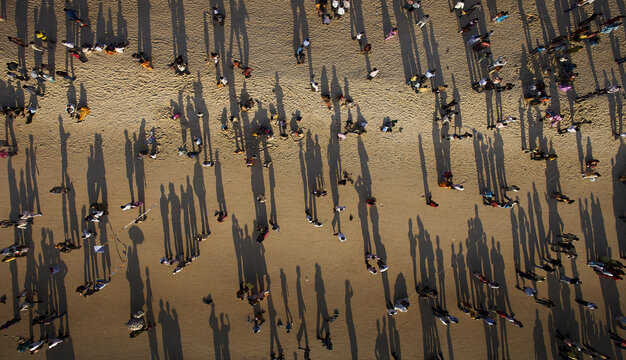 Aerial view of sunbathers cast long shadows on the sandy expanse of Panambur Beach, a lively tapestry of light and shade, Mangaluru, Karnataka, India.