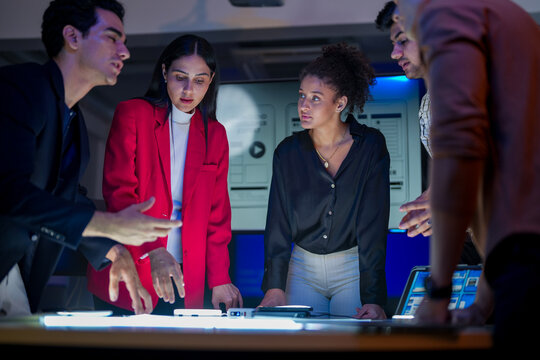 UI/UX design team conducting a workshop to review mobile app prototypes. Front-end developers and visual artists discussing web layout strategy on a large screen in a modern tech startup office. - Powered by Adobe