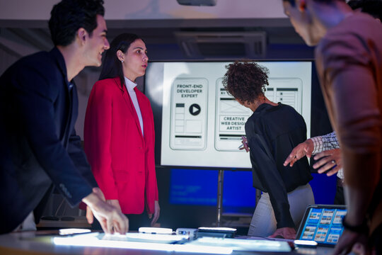 Creative UI/UX design team analyzing mobile app wireframes on illuminated digital touch table. Diverse developers brainstorming web layout strategy in modern high-tech office at night. - Powered by Adobe