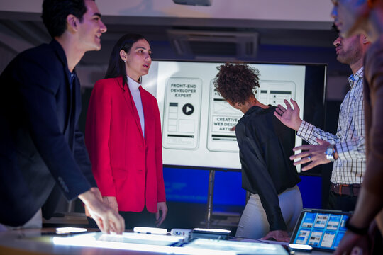 Creative UI/UX design team analyzing mobile app wireframes on illuminated digital touch table. Diverse developers brainstorming web layout strategy in modern high-tech office at night. - Powered by Adobe