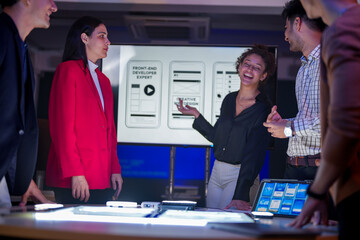 Creative UI/UX design team analyzing mobile app wireframes on illuminated digital touch table. Diverse developers brainstorming web layout strategy in modern high-tech office at night.