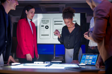 Creative UI/UX design team analyzing mobile app wireframes on illuminated digital touch table. Diverse developers brainstorming web layout strategy in modern high-tech office at night.