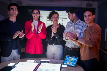 Professional software development team applauding for project success. Happy diverse group clapping hands to celebrate mobile app launch in high-tech startup office.