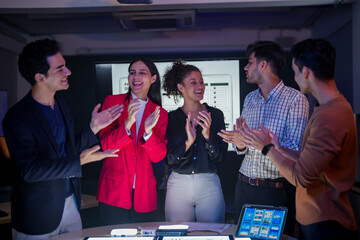 Professional software development team applauding for project success. Happy diverse group clapping hands to celebrate mobile app launch in high-tech startup office.