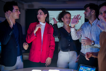 Successful creative team celebrating project achievement in modern office. Happy diverse developers high-fiving after mobile app launch during late night meeting.