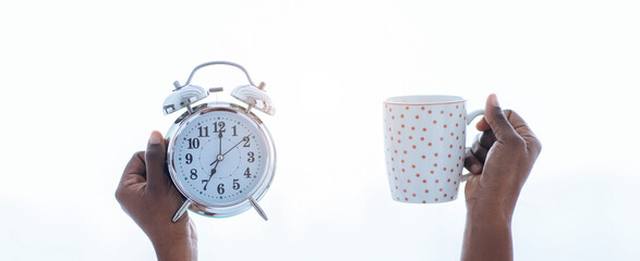 Two hands are shown, one holding a silver alarm clock and the other holding a polka dot coffee mug. The background is bright and hints at a morning setting, suggesting the start of a new day.