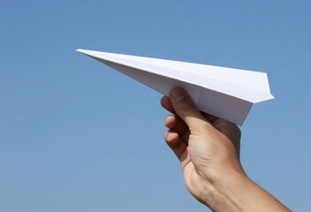 A person's hand gracefully launches a simple white paper airplane against a clear blue sky, symbolizing childhood dreams, freedom, and the joy of flight