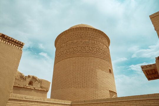 Historical Pir-e Alamdar brick tower with elaborate brick ornaments on a background of cloudy blue sky. The building is located in Damghan City Iran.